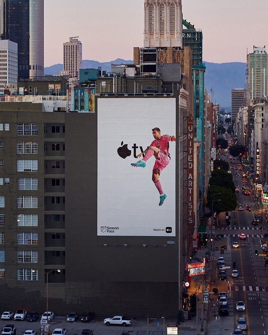 An Apple TV MLS Season Pass billboard on the side of a building in downtown Los Angeles at dusk.